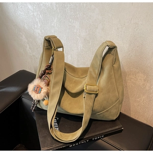 Detail of olive green suede dumpling bag featuring vintage metal buckle and plush charm