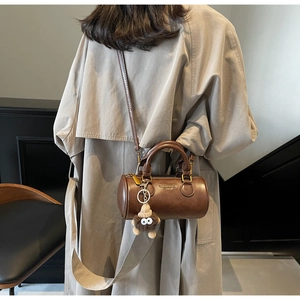 Detail of dark brown cylinder Boston bag with plush monster charm and adjustable strap