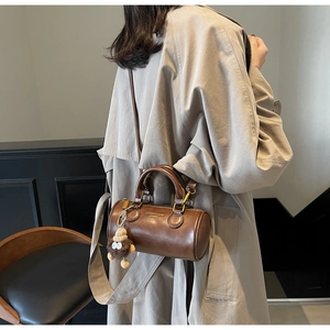 Brown cylinder handbag with plush charm shown with a trench coat on a model