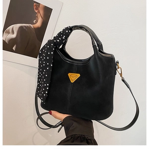 Détail d'un sac à main noir mat avec logo triangulaire et décoration d'écharpe à pois