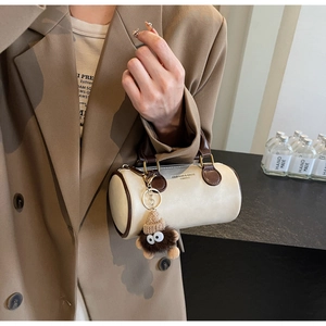 Detail of a creamy cylinder mini Boston bag with brown handles and a plush monster charm