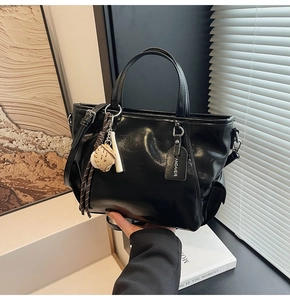 Detail of glossy black tote bag with side pocket, adjustable strap and decorative charms