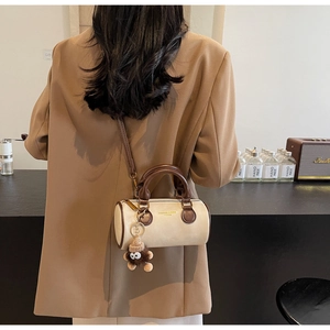 Detail of a retro cream cylinder bag with brown trim and a plush charm on a model