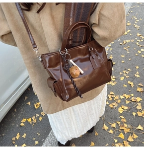 Detailed close-up of dark brown leather tote bag with a football charm on autumn leaves