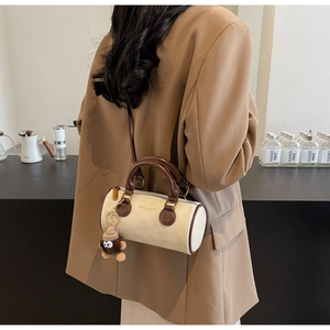 Detail of a cylindrical cream and brown crossbody bag with a plush monkey charm on a model