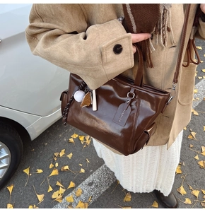 Detail of dark brown patent leather tote bag with baseball pendant and shoulder strap