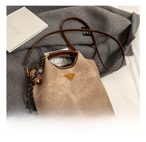 Détail du sac seau en daim kaki avec passepoil en cuir, badge et breloque en forme de cloche
