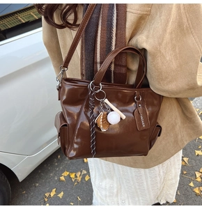 Detail of dark brown glossy tote bag with baseball charms and removable strap on model