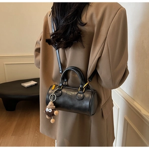 Detail of black cylindrical bucket bag with gold zipper and brown plush eye charm