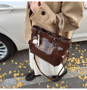 Detail of glossy brown leather tote bag with baseball charm on a leafy autumn street