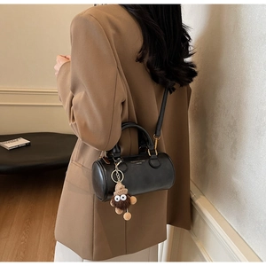 Detail of a black leather cylinder bag with a brown plush monster charm and gold accents