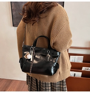 Detail of black glossy leather tote bag featuring a unique baseball charm and side pocket
