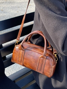 Vintage brown leather boston bag with dual handles and logo detail on outdoor background
