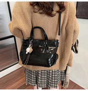 Detailed close-up of glossy black tote bag with shoulder strap and cartoon charm