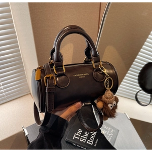 Detail of dark brown cylindrical crossbody bag with gold hardware and plush monkey charm