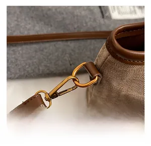 Détail du crochet en métal doré et de la bandoulière en cuir brun sur le sac en toile