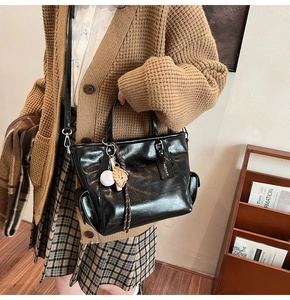 Detail of black faux leather tote bag featuring a baseball glove charm and side zipper