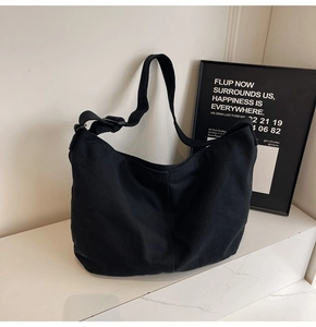 Detailansicht einer schwarzen Canvas-Hobo-Tasche mit breitem Gurt auf Marmoroberfläche