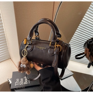 Detail of dark brown barrel bag with gold hardware and a cute brown fuzzy charm
