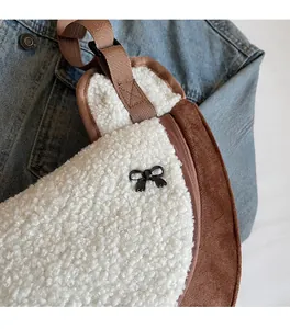 Close-up of white plush crossbody bag with brown suede trim and black metal bow detail