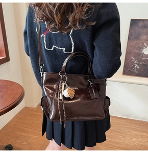 Detail of dark brown glossy patent leather tote bag with side pockets and sports pendant
