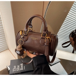 Close-up of a dark brown cylindrical handbag with golden hardware and a plush charm