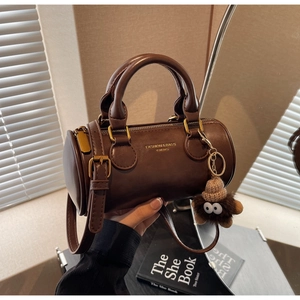 Close-up of retro brown leather cylinder bag featuring a cute plush doll charm detail