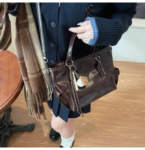 Detail of dark brown glossy tote bag with baseball themed charms and leather texture
