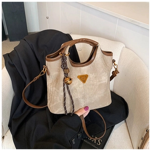 Détail du sac cabas en toile avec garniture en cuir marron et logo métal sur chaise
