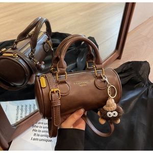 Detail of a brown cylindrical handbag with plush monster charm and top zipper closure