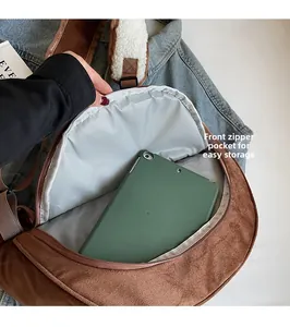 Front zipper pocket of brown suede dumpling bag storing a tablet with green case