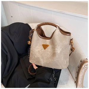 Détail d'un sac cabas beige avec bordure en cuir marron et logo doré sur une chaise