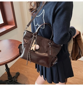 Detail of a shiny dark brown tote bag with a baseball charm and premium brand tag