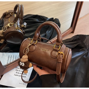 Detailed mirror view of dark brown cylindrical crossbody bag with plush charm and leather texture