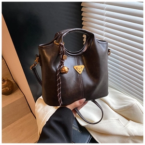 Détail d'un sac cabas en cuir mat marron foncé avec logo doré et pendentif tressé