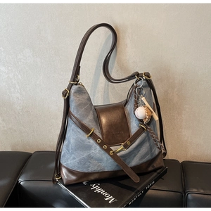 Detailed view of tote bag with blue textured fabric, leather accents and baseball charm