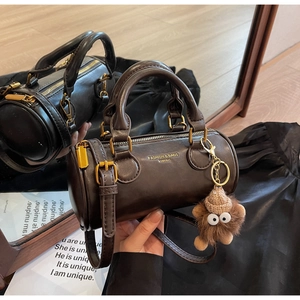 Detailed mirror view of brown leather cylinder handbag with plush monster charm
