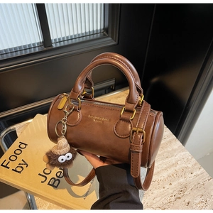 Detailed view of dark brown cylinder bag with gold lettering and plush monster charm