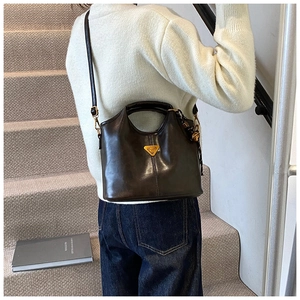Détail d'un cabas en cuir marron foncé avec logo triangulaire doré et anse élégante