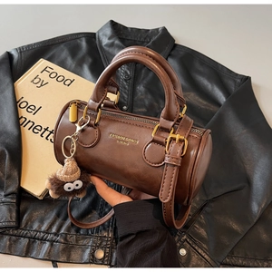 Detailed close-up of dark brown leather cylinder bag with plush bear charm and shoulder strap