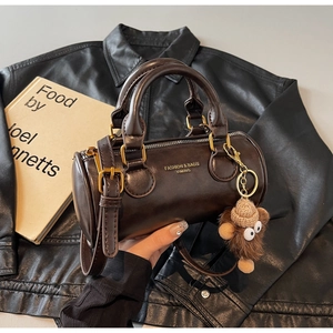 Detail of dark brown cylinder handbag featuring a monkey charm and gold hardware