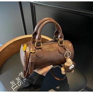 Brown cylinder Boston bag detail with plush monster charm and gold hardware accents