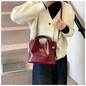 Sac fourre-tout bordeaux avec logo doré porté par un mannequin dans un cadre épuré