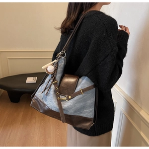 Detail of blue canvas tote bag with brown leather straps and baseball charm accessory