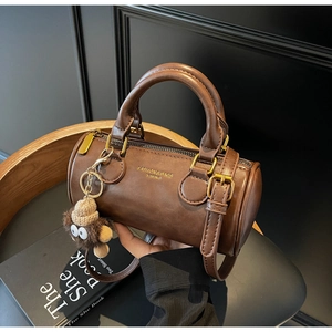 Close-up of brown leather cylinder handbag with cute lion charm and adjustable strap