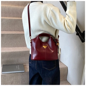Détail du sac fourre-tout en cuir rouge foncé avec logo triangle doré et bandoulière
