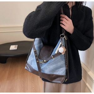 Side view of large denim tote bag with vintage leather trim and baseball charms on model