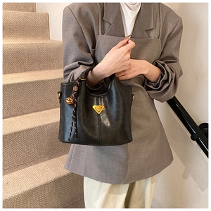 Détail d'un sac cabas en cuir noir avec logo triangulaire doré et breloque tressée