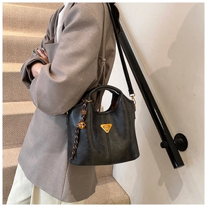 Détail d'un sac cabas en similicuir noir avec logo triangle doré sur un escalier gris