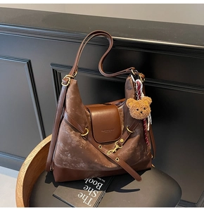 Detailed view of brown suede hobo bag with teddy bear charm on leather chair
